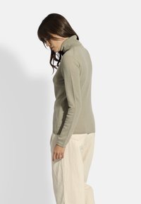 Maglione a collo alto aderente di colore grigio chiaro, realizzato in materiale morbido, con maniche lunghe e una fine trama a costine lungo il collare e l'orlo.