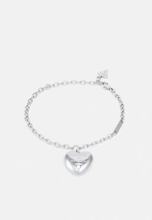 Bracelet chaîne en argent avec un pendentif en forme de cœur gravé "GUESS is for lovers" et un petit cristal clair incrusté sous le texte.