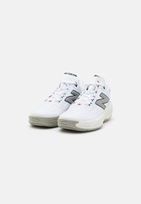 Zapatillas deportivas blancas con una parte superior texturizada, que presentan un gran logo "N" gris, acentos rojos y un diseño de suela acolchada.