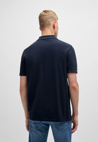 Marinblå polo skjorta i bomull, med korta ärmar, klassisk krage och rak nederkant. Sedd bakifrån. Bärs tillsammans med blå jeans.