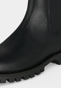 Gros plan d'une botte en cuir noir avec une semelle extérieure texturée et un panneau latéral élastique pour un chaussage facile.