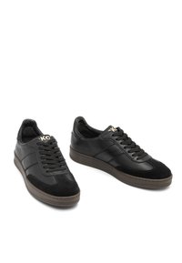 Un paio di sneakers nere in pelle con punte in suede, lacci neri e suole in gomma marrone, posizionate con una scarpa leggermente dietro l'altra.