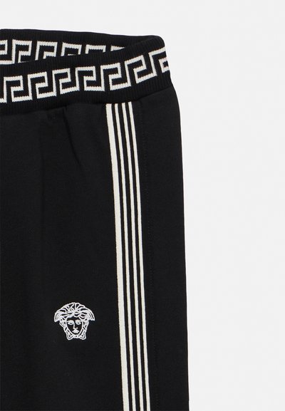 Black pants with white vertical stripes and Greek key patterned waistband, featuring a white Medusa head logo on the thigh.