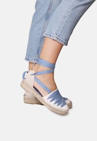 Espadrillas blu e bianche con suole in juta intrecciata e nastri. Presentano un design a intaglio nella parte anteriore e legacci alla caviglia.