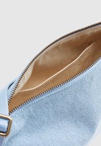 Φωτεινή μπλε τζιν θήκη με εσωτερικό από μπεζ ύφασμα και ανοιχτό φερμουάρ, που αποκαλύπτει μια μικρή εσωτερική τσέπη και μεταλλικό κούμπωμα στο λουρί.