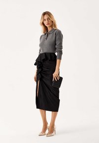 Maglione grigio lavorato a maglia con colletto, gonna nera a balze con uno spacco, tacchi alti dorati e una pochette nera a trama.