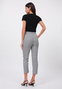 Svart ribbad kortärmad topp i kombination med grå rutiga tapered-byxor, som har elastisk midja och ankellång fåll. Svarta remsandaler.