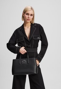 Black structured handbag made of textured material, featuring dual handles and a white embossed logo detail on the front.