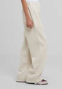Pantaloni della tuta a gamba larga color crema con tasche laterali e vita elastica, abbinati a scarpe multicolori. Tessuto morbido, vestibilità comoda.