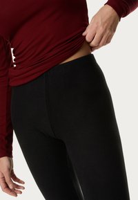 Zwarte leggings van rekbaar materiaal hebben een hoge taille en een soepele textuur. Een aansluitende snit accentueert de lichaamscontour.