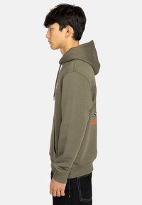 Haut à capuche vert olive en tissu doux, avec une poche kangourou et un cordon de serrage ; comprend des graphismes brodés en orange et noir.