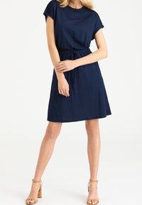 Vestido azul marino con mangas cortas y acentos texturizados en los hombros. Presenta una cintura con cordón para un ajuste ajustable y una falda acampanada.