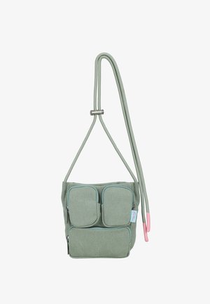Small green fabric crossbody bag with three zippered pockets and adjustable cord strap featuring pink end caps.