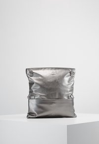 Metallinhohtoinen hopeanvärinen laukku, jossa pehmeä pinta, säädettävät hihnat ja taitettava yläosa. Ominaisuuksia ovat sileä, kiiltävä materiaali ja minimalistinen muotoilu.