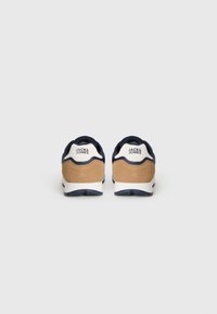 Navy sneakers with a suede tan heel accent, white logo, textured upper, and a thick white sole. Designed for comfort and stability.