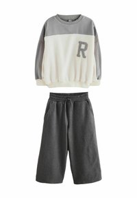 Dvoslojni komplet, ki vključuje sivi in smetankasti flis pulover z teksturirano površino ter sive hlače s elastičnim pasom.