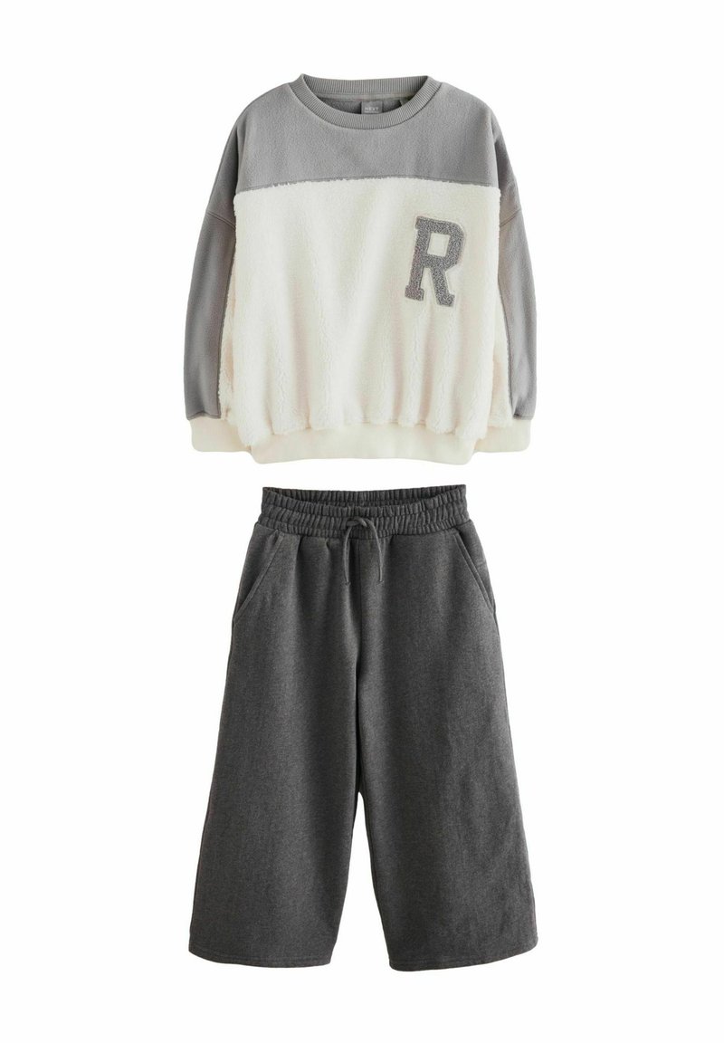 Dvoslojni komplet, ki vključuje sivi in smetankasti flis pulover z teksturirano površino ter sive hlače s elastičnim pasom.
