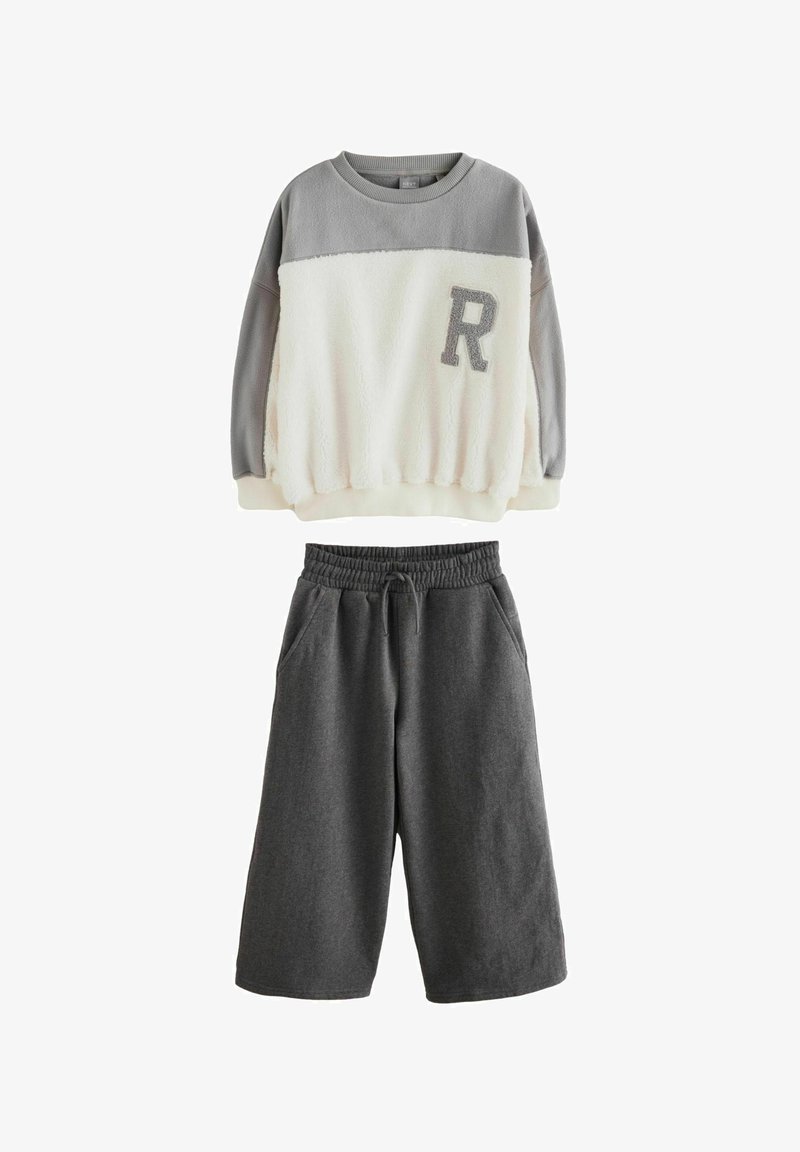 Dvoslojni komplet, ki vključuje sivi in smetankasti flis pulover z teksturirano površino ter sive hlače s elastičnim pasom.