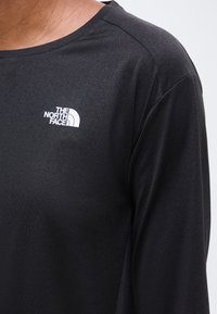 Μαύρο πουκάμισο με μακριά μανίκια που φοριέται από άτομο, με λευκό λογότυπο "The North Face" στο αριστερό στήθος.