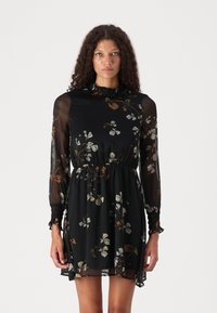 Rochie neagră cu flori, cu mâneci lungi din material transparent, decolteu volanat, talie elastică și croi lejer cu tiv fluid.
