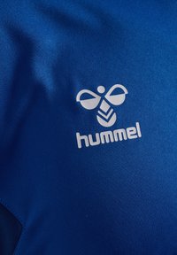 Blåt tekstil med en glat, blød overflade. Et hvidt logo med en stiliseret bi og ordet "hummel" trykt nedenfor.