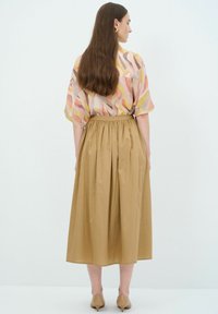 Blusa fluida multicolore con motivi a onde pastello; gonna alta in vita di un solido color sabbia; texture liscia; lunghezza a metà polpaccio; scarpe beidge.