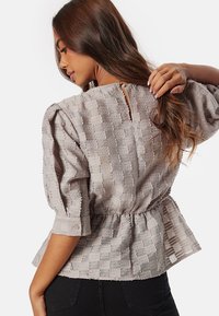 Blusa grigia, strutturata, con maniche a sbuffo, scollo rotondo e chiusura con bottoni posteriori. Vita arricciata e dettagli a righe sottili.