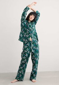Lilleline pidžaama komplekt rohelise ja sinise tooni koosseisus, sisaldades nööbiga pluusi ja lahtisi pükse, millel on abstraktsed lehe- ja lillemustrid.