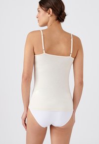 Camisole beige chiaro con spalline sottili e regolabili, texture liscia, design aderente e orlo semplice, abbinata a slip bianchi.