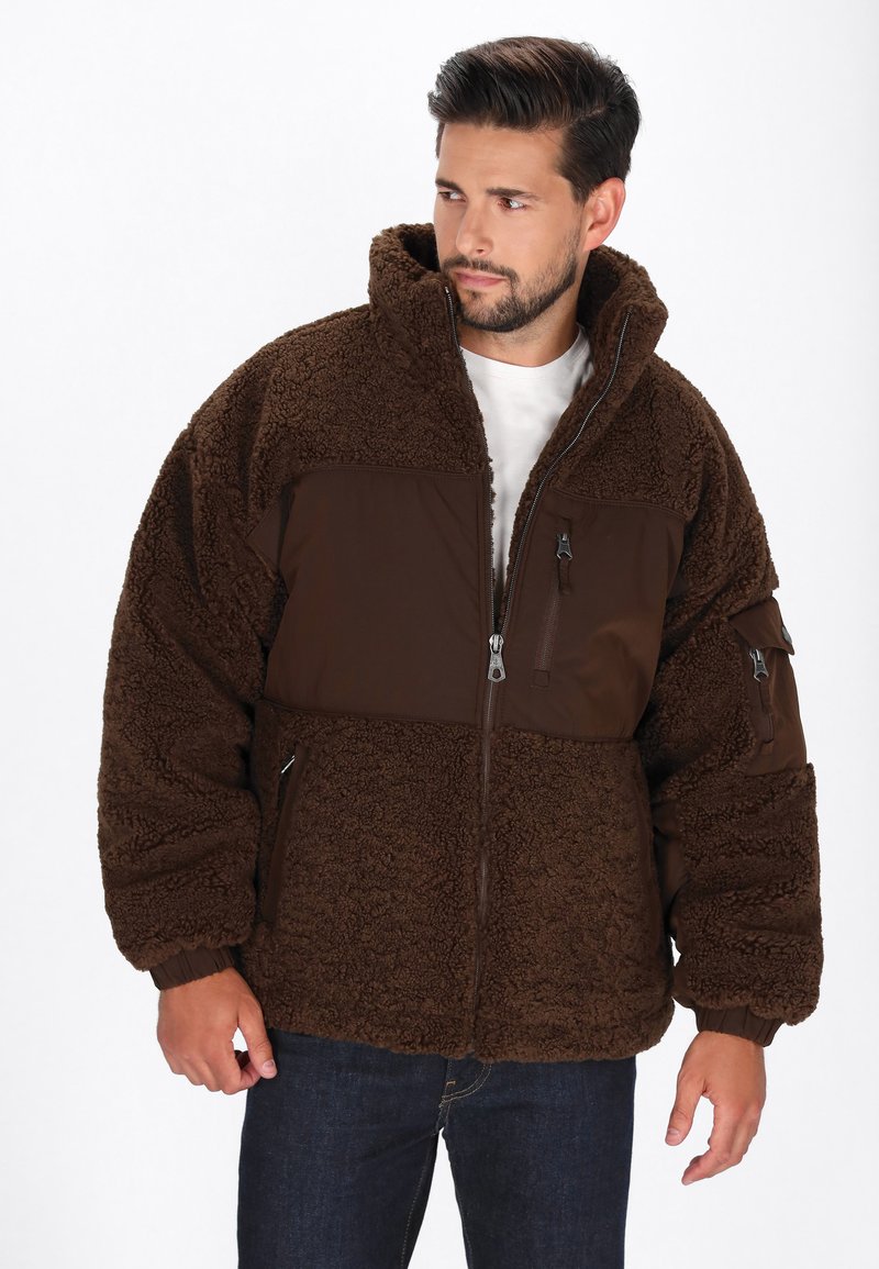 Braune Fleecejacke mit Reißverschlussfront und Kapuze. Sie verfügt über ein glattes Oberteil, Seitentaschen und elastische Bündchen. Texturiert und warm.
