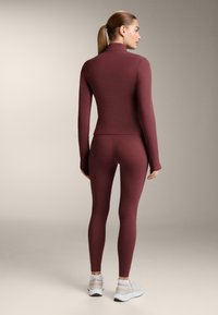 Bordo sportski komplet koji se sastoji od uske dugih rukava i tajica. Glatki, rastezljivi materijal s bešavnim dizajnom i minimalističkim stilom.