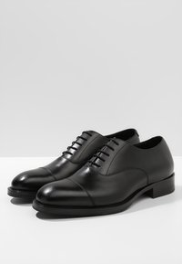 Chaussures en cuir noir avec bout arrondi, finition lisse, détail lacé et petit talon empilé. Design simple, forme classique.