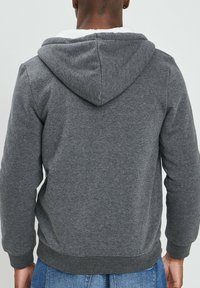 Sudadera gris con una capucha suave forrada de felpa blanca, puños y dobladillo acanalados. El material parece suave, con un corte casual y sin patrones visibles.