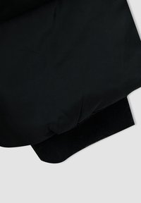 Esquina de chaqueta acolchada negra con tela de nailon suave, puño elástico con textura acanalada y costuras visibles.