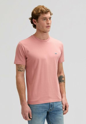 Maglietta di cotone rosa con scollo rotondo, maniche corte e piccolo logo nero sul petto a sinistra. Vestibilità classica, tessuto liscio.