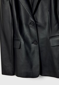 Blazer en cuir noir avec deux boutons et poches à rabat, présentant une texture lisse et des détails de couture sur mesure.