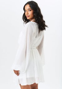 White dress with sheer, textured fabric, long billowy sleeves, and a cinched waist. Features subtle metallic details throughout.