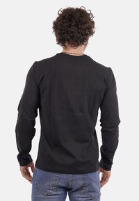 T-shirt nero a maniche lunghe con scollo rotondo, texture liscia e dettagli di cucitura minimi. Abbinato a jeans blu.