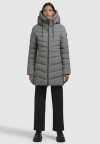 Lichtgrijze gewatteerde jas met een capuchon, voorzien van een voorkeursrits, verticale quilting en een slim fit, in combinatie met zwarte broeken.