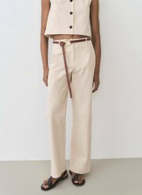 Beige kort topp med svarta knappar, kombinerad med högmidjade, raka beiga byxor och ett brunt läderbälte med en cirkulär spänne.