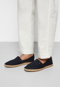 Espadrillas in tela di colore blu navy con suola in juta intrecciata e bordo cucito, caratterizzate da un piccolo logo decorativo sul lato.