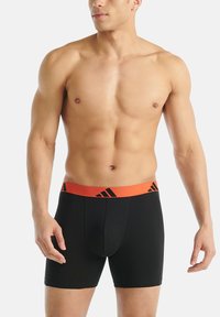 Černé boxerky s oranžovým páskem, vyznačující se černými logy, vyrobené z hladké, elastické látky, střih přiléhající k tělu.