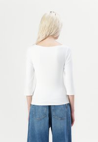 Hvit langermet topp med bred hals og trekvart ermer, kombinert med høy midje blå denim vide benbukser. Glatt tekstur.