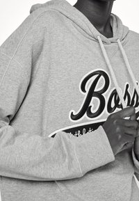 Grey pullover hoodie featuring a large black "Boss" logo, a drawstring hood, and ribbed cuffs with a soft, textured fabric.