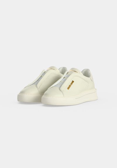 Paire de baskets slip-on blanc cassé avec semelles épaisses et bandes élastiques remplaçant les lacets, marquées "roberto cavalli" en lettres dorées sur les côtés.