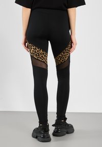 Leggings neri con pannello a stampa leopardata e dettagli in rete lungo i lati. Texture liscia e design aderente. Indossati con sneaker nere.