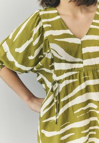Grün-weiß gestreiftes Kleid mit V-Ausschnitt, kurzen Puffärmeln, elastischem Taillenzug und verstellbarem Bindedetail. Aus leichtem Stoff gefertigt.