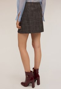 Grijze geruite minirok met een rechte snit, gecombineerd met glanzende bordeauxrode enkellaarsjes met een vierkante hak en decoratieve gespdetails.