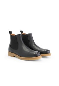 Zwarte leren Chelsea boots met elastische zijpanelen, ronde neus en beige rubberen zool. Voorzien van trekloops voor gemakkelijke aan- en uittrekken.
