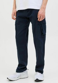 Marinblå cargobyxor i tåligt tyg, med flera fickor, en avslappnad passform och slät yta. Kombinerade med vita sneakers.